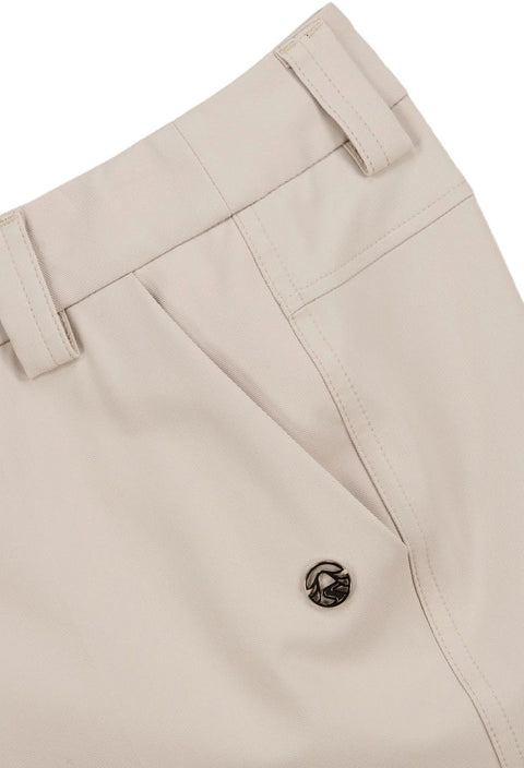 Detailaufnahme einer cremefarbenen Hose mit Fokus auf die Vordertaschen, Nähte und einen metallischen Button mit graviertem Logo