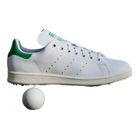 Weißer Adidas Stan Smith Golfschuh auf Golfrasen mit Golfball und Fahne im Hintergrund